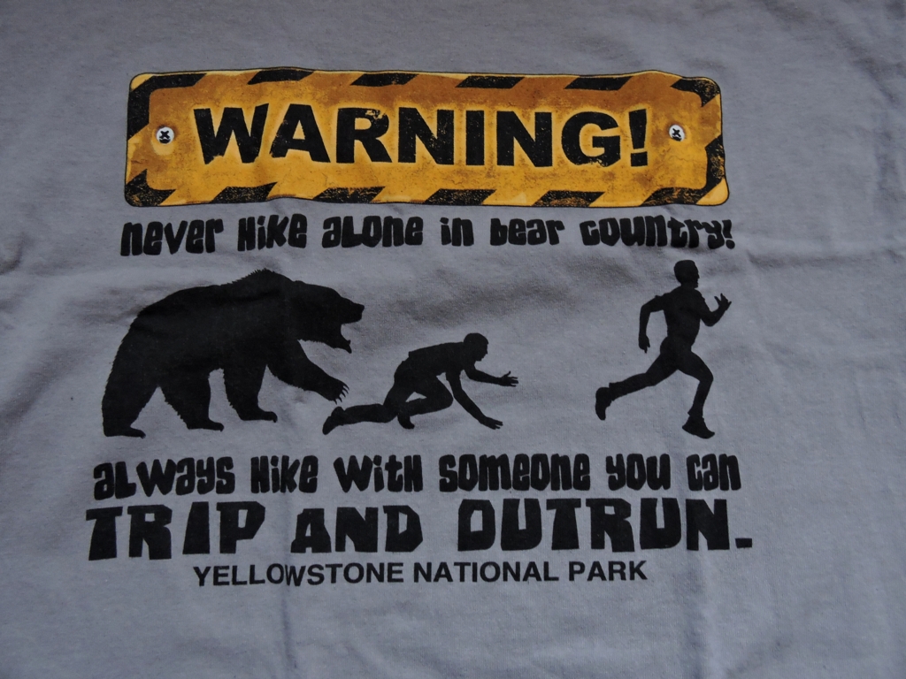 Fragment koszulki z Yellowstone: "ostrzeżenie - nigdy nie wędruj sam w krainie niedźwiedzi, zawsze wędruj z kimś kto może się potknąć i kogo można prześcignąć".